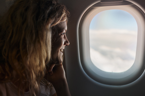 Young happy woman looking through window while traveling by airplane.