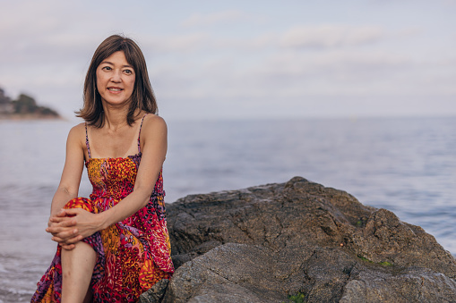 Portrait of a japanese woman on a beach sitting on a rock