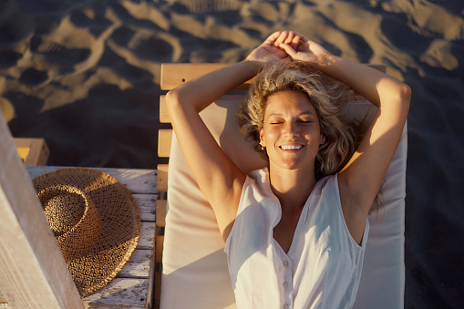 High angle view of happy woman enjoying while resting on deck chair with her eyes closed.