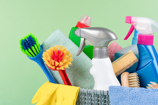Closeup view of cleaning household supplies against green background. Cleaning service concept. Spray bottles with detergents and household chemicals