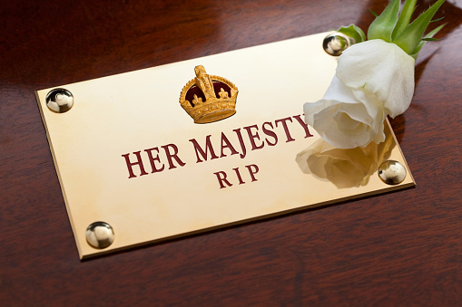 A memorial brass plaque bearing a gold crown on a mahogany coffin with engraved the text, Her Majesty, R.I.P, Rest in Peace, with a single white rose.