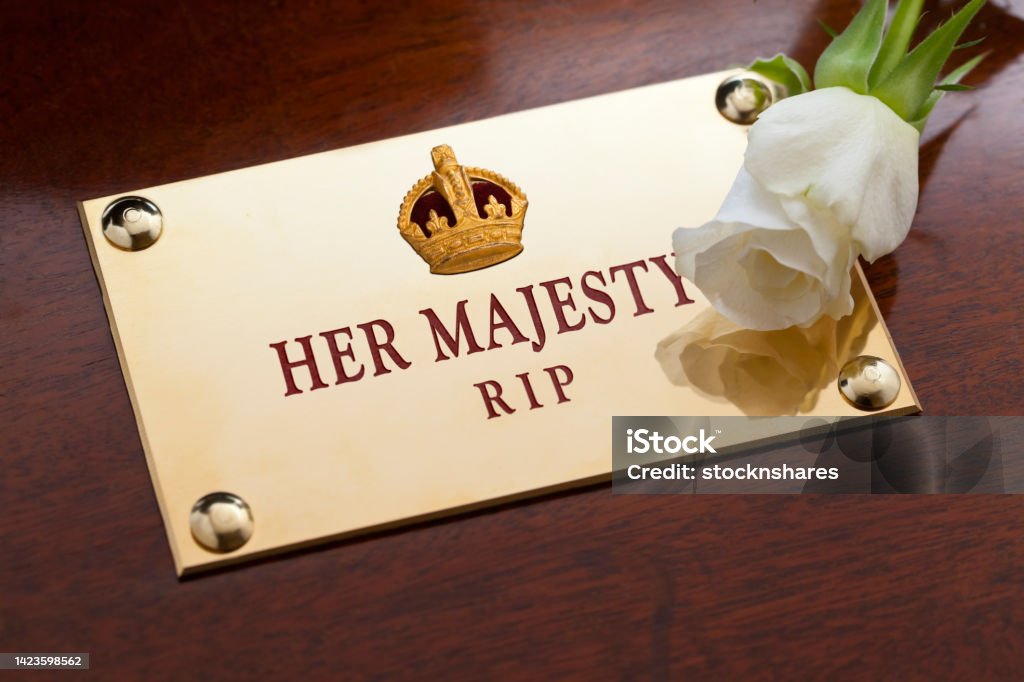 Her Majesty Rest in Peace A memorial brass plaque bearing a gold crown on a mahogany coffin with engraved the text, Her Majesty, R.I.P, Rest in Peace, with a single white rose. Funeral Stock Photo