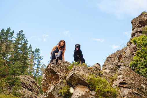 Hiker woman sitting on a rock with her dog taking a break while trekking through the mountains. travel with pet concept