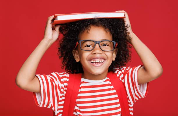 Happy ethnic schoolboy laughing and playing with book