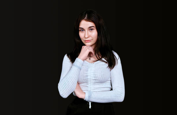 istock Slender young brunette in white blouse with large breasts, propping her head with her hand, looks thoughtfully into camera, posing on black background. Banner, place for text. 1423602635