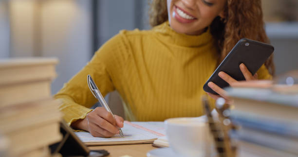 Writing notes, learning books and study of a woman university student with a phone. College education of a female with a happy smile and scholarship preparing for a exam, test or book report