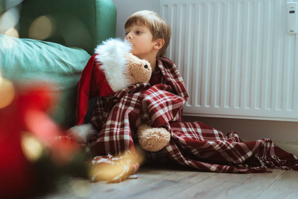 istock cute little boy wrapped id plaid sitting by heater 1423602747