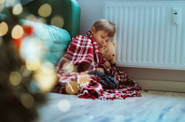 istock cute little boy wrapped id plaid sitting by heater 1423603157