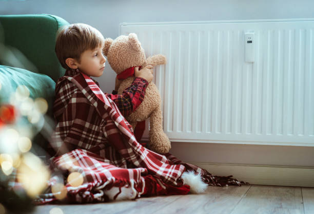 istock cute little boy wrapped id plaid sitting by heater warming teddy bear paws 1423603292