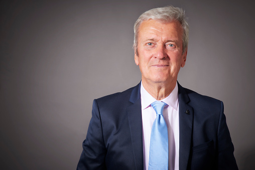 Closle-up studio portrait of grey haired businessman wearing suit while standing at isolated grey background. Copy space.
