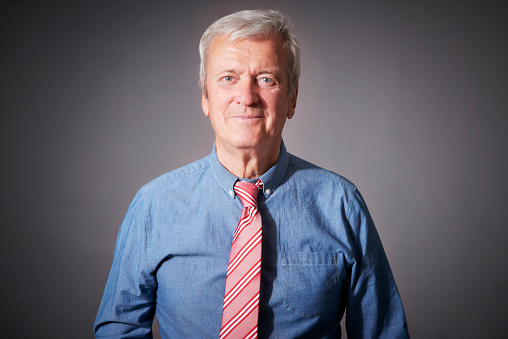 Studio portrait of senior businessman wearing shirt and tie while standing at isolated grey background.