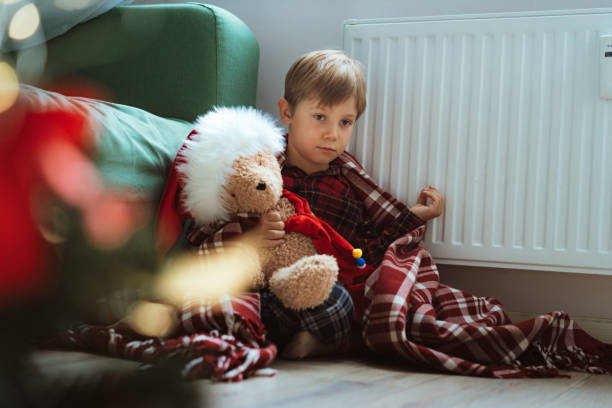 istock cute little boy wrapped id plaid sitting by heater 1423604289