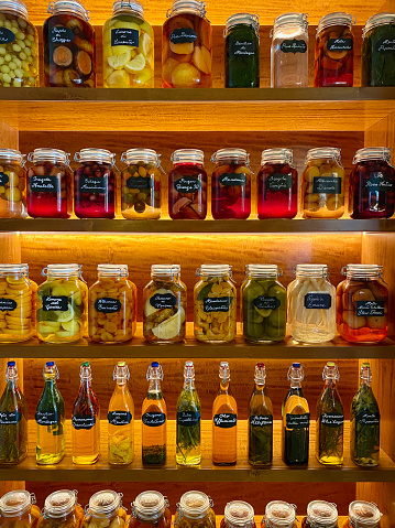 Shelf with various coloured pickled vegetables an fruits, vegetarian and vegan food in jars neatly ordered in rows on wooden shelves for conservation in a restaurant in Venice, Italy