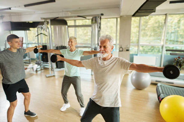 istock Senior couple exercising with personal trainer using dumbbells at the gym 1423608077
