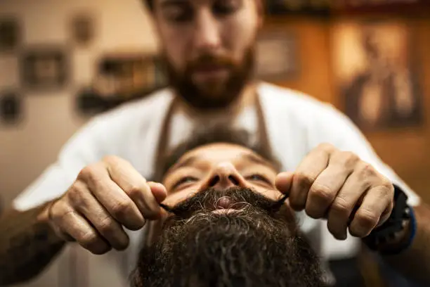 Photo of Barber styling mustaches of a customer in barber shop