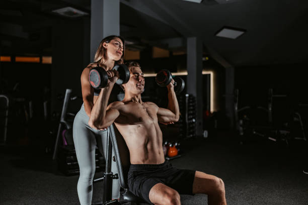 istock Young Female Trainer Helping Young Man With Lifting Weights In The Gym 1423614708