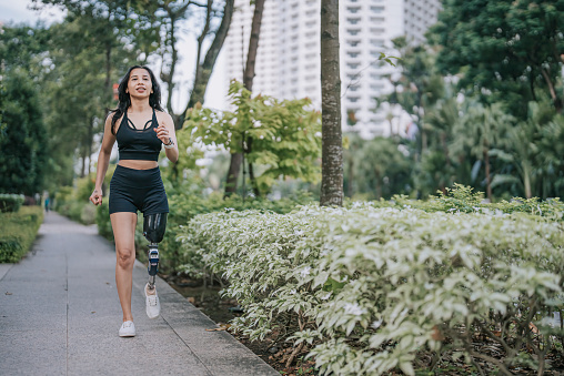 Asian female athlete with disability artificial leg jogging at pedestrian walkway in the morning