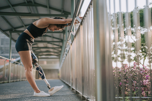 Asian female athlete with disability artificial leg warm up stretching at pedestrian walkway bridge before jogging in the morning