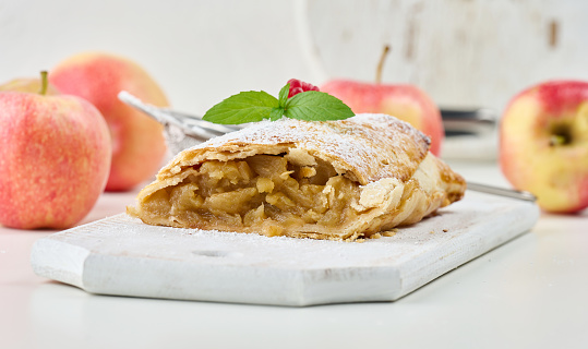 Baked strudel with apples sprinkled with powdered sugar on a white wooden board, delicious dessert