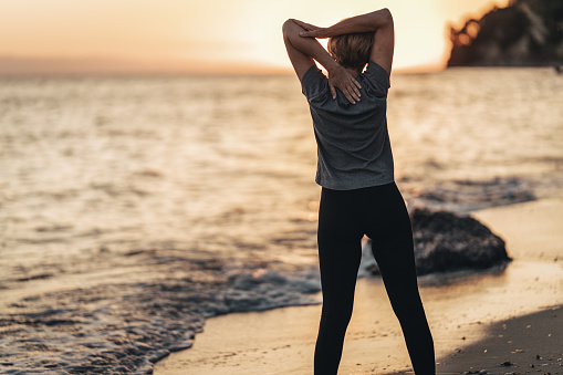 Mature woman exercising alone on the beach by the sea in sunset.