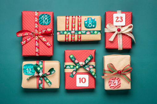 Handmade wrapped red, green gift boxes decorated with ribbons, snowflakes and numbers, Christmas decorations and decor on green table Xmas advent calendar concept Top view Flat lay Holiday card.