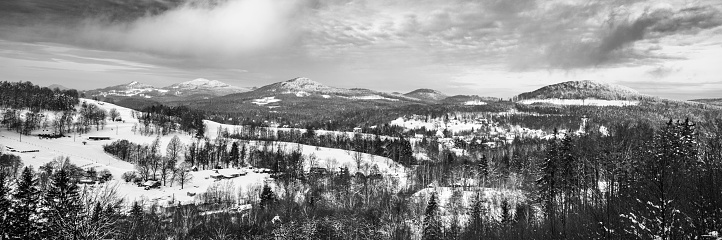Snowy winter hilly landscape. Beautiful rural range. Panorama with Kytlice village in Lusatian Mountains, Czech Republic. Black and white image.