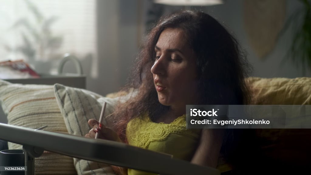 Woman with a disability drawing on tablet Concentrated woman with spinal muscular atrophy sitting on a couch at cozy home and drawing on digital tablet computer using pencil 35-39 Years Stock Photo