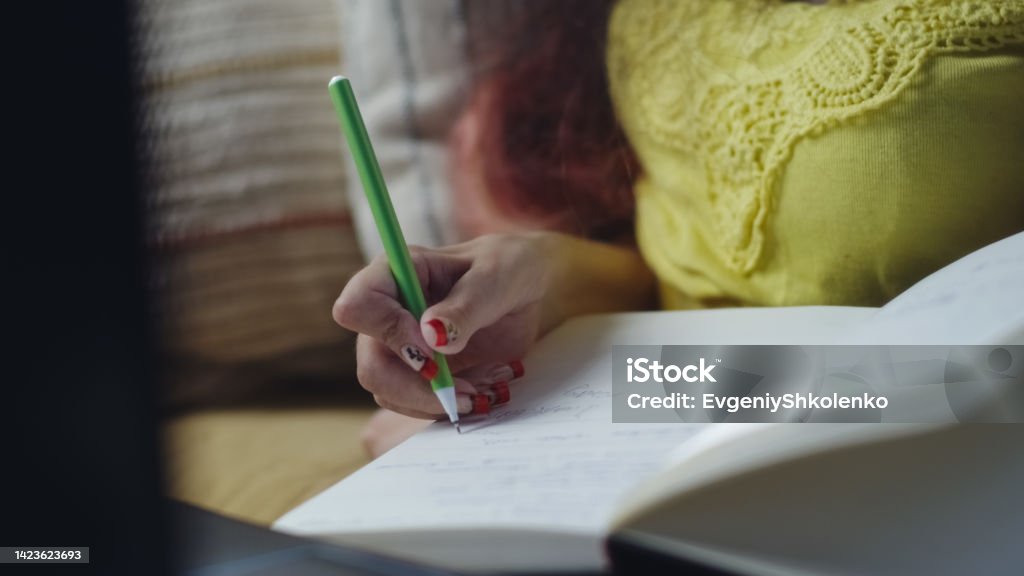 Woman with a disability writing in notebook Woman with spinal muscular atrophy sitting on a sofa at home and making notes in notebook during online studying using laptop One Person Stock Photo