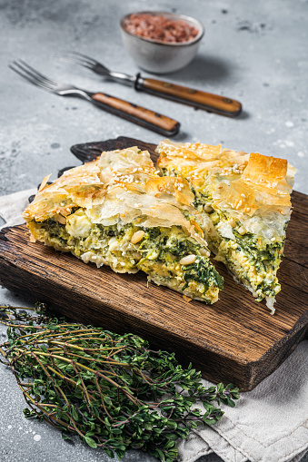 Greek Pie Spanakopita with Spinach and Cheese on wooden board. Gray background. Top view.