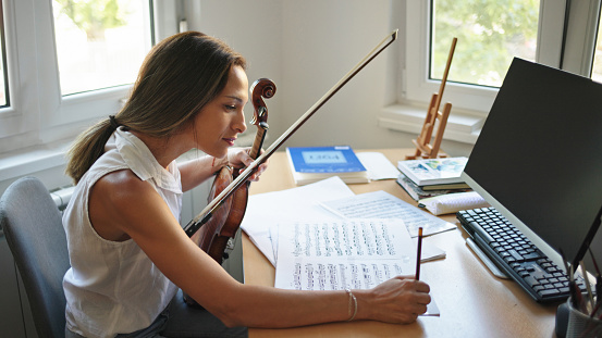Female violinist practicing playing violin by reading sheet music at home