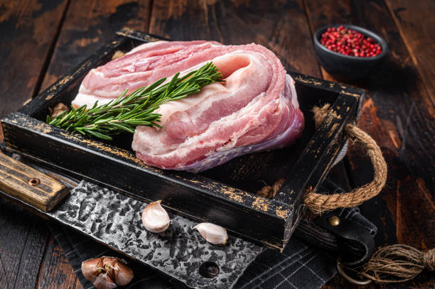 Organic uncooked Pork belly, raw bacon meat in a wooden plate with thyme. Wooden background. Top view Organic uncooked Pork belly, raw bacon meat in a wooden plate with thyme. Wooden background. Top view. berkshire pig stock pictures, royalty-free photos & images