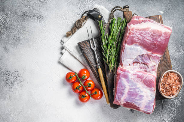 Pork belly block, raw meat with skin on a wooden board with rosemary. White background. Top view. Copy space Pork belly block, raw meat with skin on a wooden board with rosemary. White background. Top view. Copy space. berkshire pig stock pictures, royalty-free photos & images