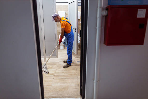 A side view of a mature school janitor mopping the floor of a public toilet and disinfecting and preventing illness.