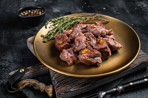 Chopped Grilled Diced Beef garlic steak on a plate with thyme. Black background. Top view.