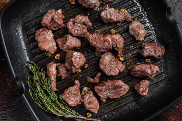 istock Diced beef cubes roasting in a grill pan for stew or goulash. Dark background. Top view 1423628841