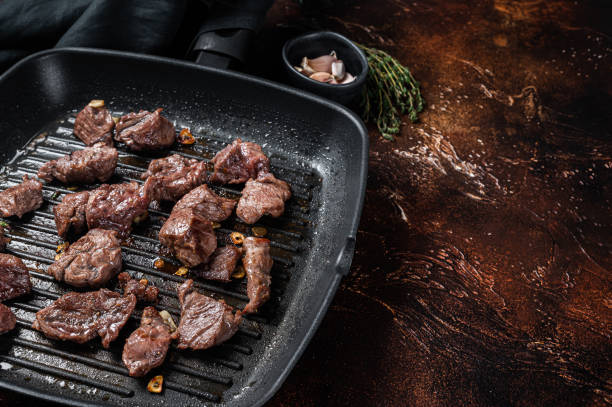 istock Diced beef cubes roasting in a grill pan for stew or goulash. Dark background. Top view. Copy space 1423628876