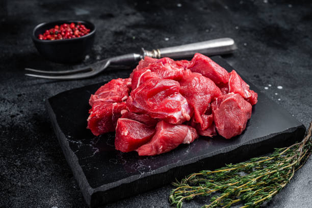 istock Raw diced red beef meat for Goulash on marble board. Black background. Top view 1423631157
