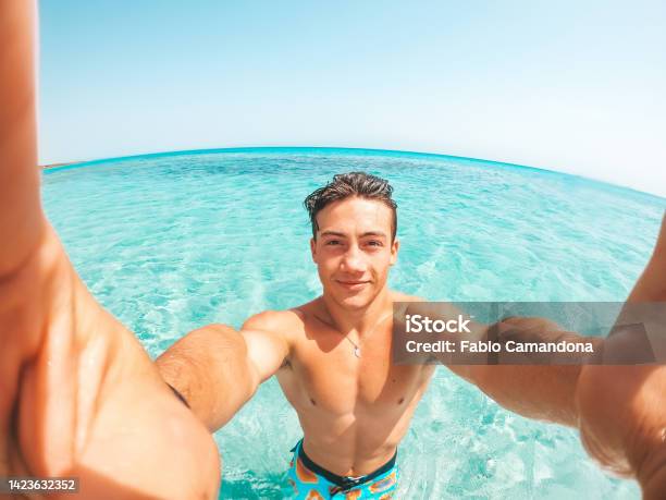 Portrait Of Happy Young Man Taking A Selfie Of Him In The Beach In A Blue Turquoise Water Having Fun And Enjoying Alone Vacations Outdoors Stock Photo - Download Image Now
