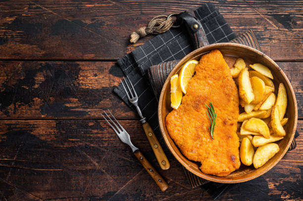 Austrian fried weiner schnitzel with potato wedges in a wooden plate. Wooden background. Top view. Copy space Austrian fried weiner schnitzel with potato wedges in a wooden plate. Wooden background. Top view. Copy space. scaloppini stock pictures, royalty-free photos & images