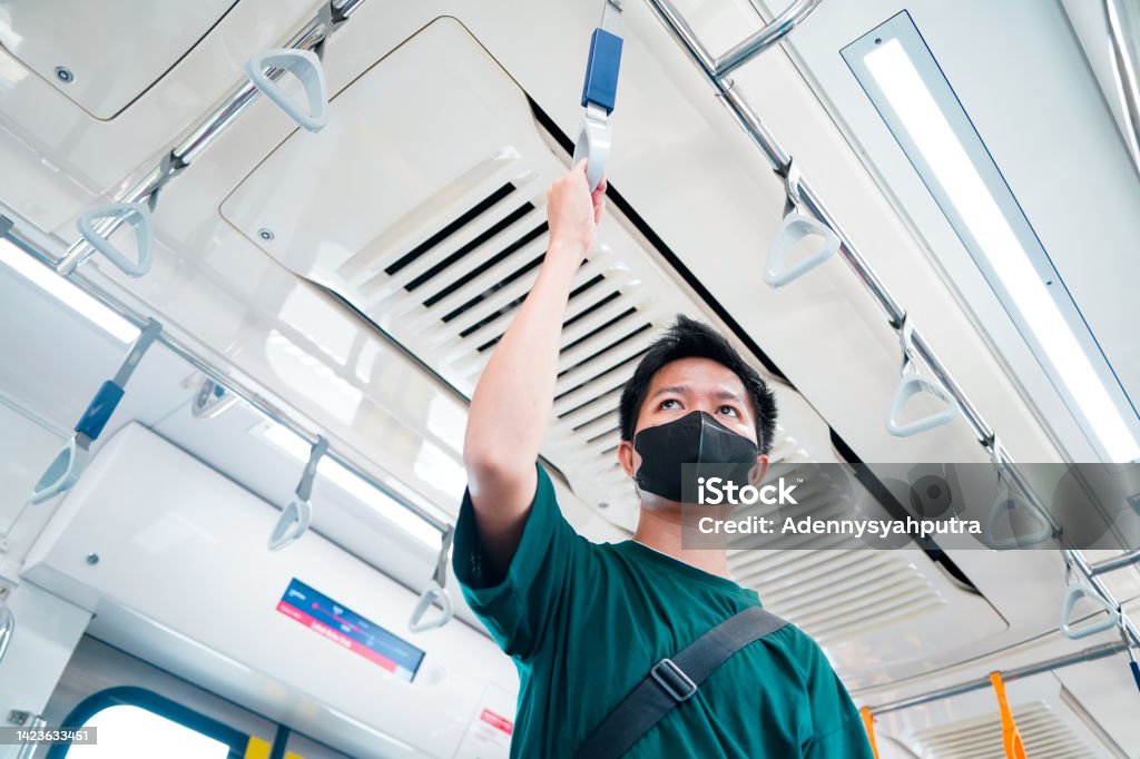 Asian passenger man wearing protective face mask and standing inside MRT Jakarta train at railway platform while traveling to work, Jakarta, Indonesia Bus Stock Photo