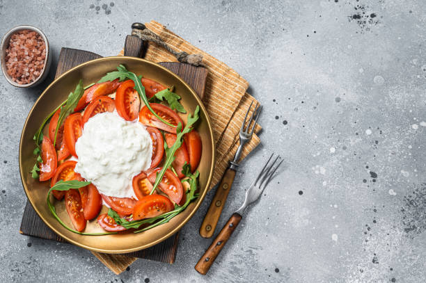 istock Italian cheese stracciatella burrata on plate with fresh tomatoes and arugula. Gray background. Top view. Copy space 1423634848