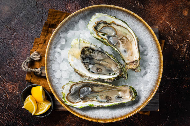istock Opened Fresh oysters with lemon and ice in a plate. Dark background. Top view 1423635534