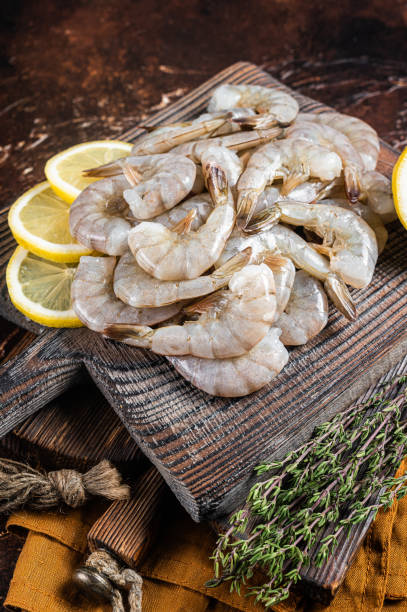 istock Raw tiger white shrimp prawn on board with herbs. Dark background. Top view 1423636108