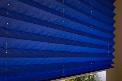 Pleated blinds XL, blue color, with 50mm fold closeup in the details on the window in the interior. Home blinds - modern bottom up privacy shades on apartment windows.