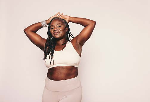Athletic woman looking at the camera while standing against a grey background. Sporty woman with dreadlocks wearing sports clothing in a studio. Mature black woman maintaining a fit lifestyle.