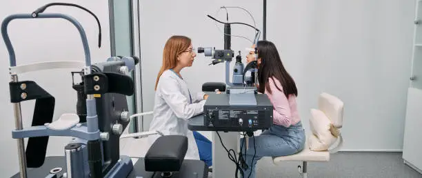 Caucasian optometrist doing sight test for Japanese woman at modern ophthalmology clinic. Eye exam and vision diagnostic