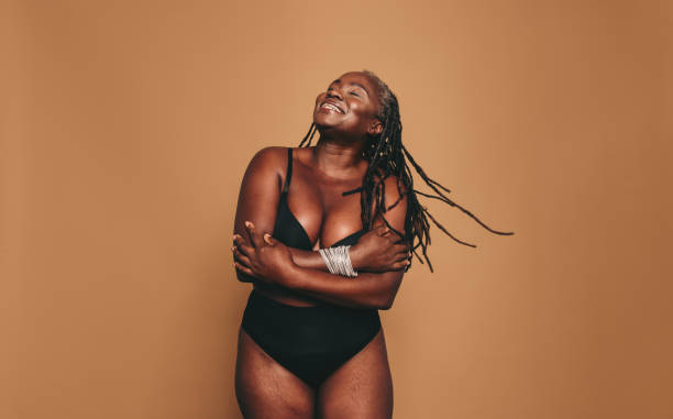 Loving my natural body Loving my natural body. Happy woman with dreadlocks embracing her natural and ageing body. Mature black woman smiling cheerfully while standing against a studio background in black underwear. bra stock pictures, royalty-free photos & images