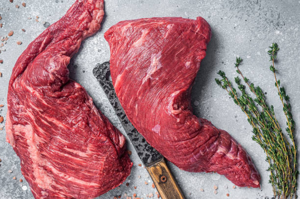 istock Unccoked tri-tip triangle roast, raw bottom sirloin steak on buther table with meat cleaver. Gray background. Top view 1423638147