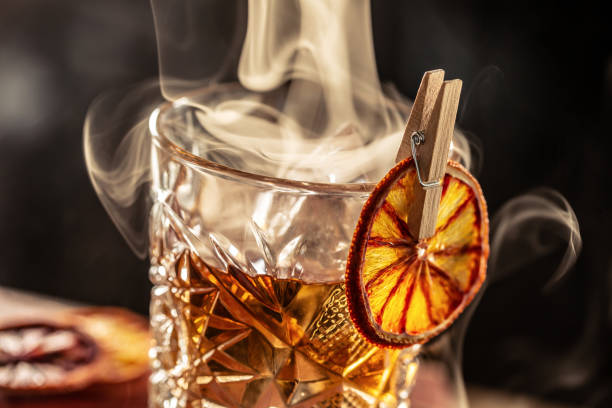 cocktail di rum vecchio stile affumicato con cubetti di ghiaccio su uno sfondo scuro. - affumicato foto e immagini stock