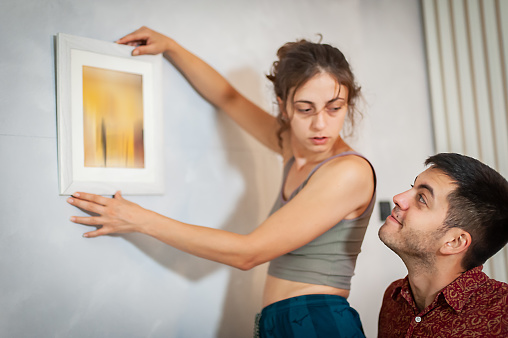 Cheerfully young couple decorates their new apartment with painting on the wall